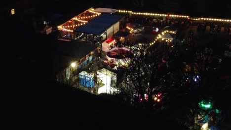 Illuminated-Christmas-fairground-festival-in-neighbourhood-car-park-at-nighttime-aerial-view