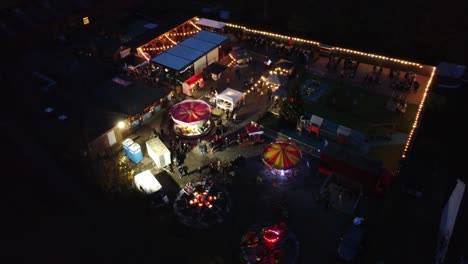 Illuminated-Christmas-spinning-fairground-rides-in-neighbourhood-car-park-at-night-aerial-view