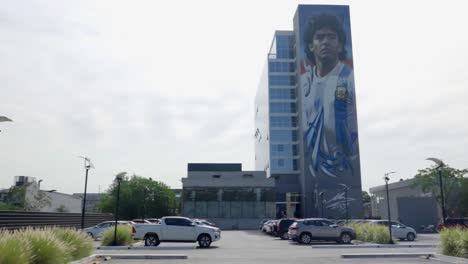 Comprehensive-Panoramic-Sweep-Across-a-City-Parking-Lot,-Revealing-a-Magnificent-Mural-of-Maradona-Gracing-the-Background