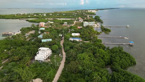 Drone-view-in-Belize-flying-over-caribbean-sea,-a-caye-covered-with-palm-trees-and-restaurants-on-a-cloudy-day
