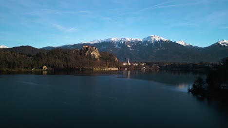 Vorwärts-Drohnenaufnahme-Mit-Der-Burg-Von-Bled,-Slowenien-Und-Den-Julischen-Alpen-Im-Hintergrund