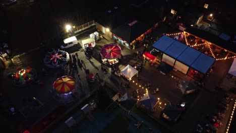Illuminated-Christmas-fairground-carnival-in-neighbourhood-pub-car-park-at-night-aerial-view