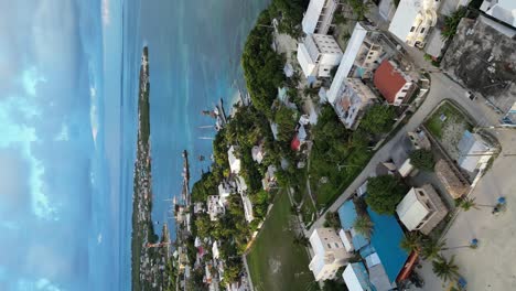 Vista-Vertical-De-Drones-En-Belice-Volando-Sobre-El-Mar-Caribeño-Azul-Oscuro-Y-Claro,-Un-Cayo-De-Arena-Blanca-Cubierto-De-Palmeras-Y-Restaurantes-En-Un-Día-Nublado
