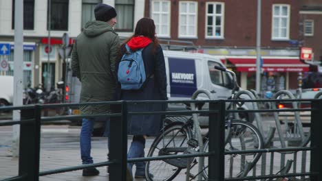 Girl-in-red-blue-outfit-and-man-stand-next-to-canal-in-Amsterdam-and-continue-walk