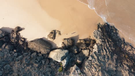 Ascending-top-down-shot-of-person-at-rocky-coastline-and-ocean-in-Portugal---Sandy-beach-during-sunny-day