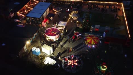 Illuminated-Christmas-funfair-festival-in-neighbourhood-pub-car-park-at-night-aerial-view