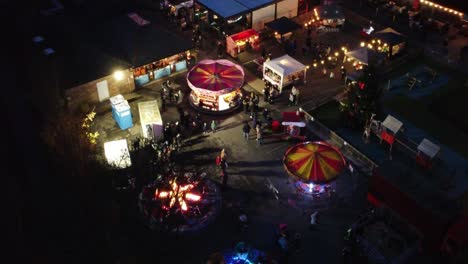 Illuminated-Christmas-fairground-attraction-in-neighbourhood-pub-car-park-at-night-aerial-view