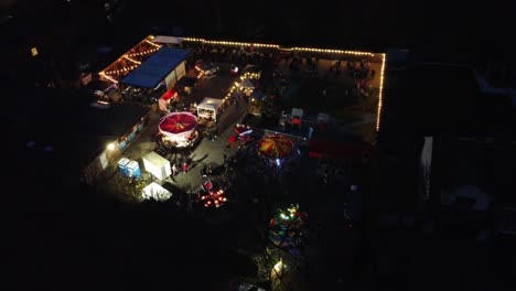 Bright-Illuminated-Christmas-fairground-festival-in-neighbourhood-car-park-at-night-aerial-view