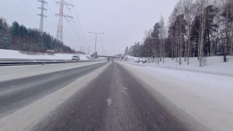 A-car-is-driving-on-a-snow-covered-freeway-road,-indicating-hazardous-travel-conditions-in-winter