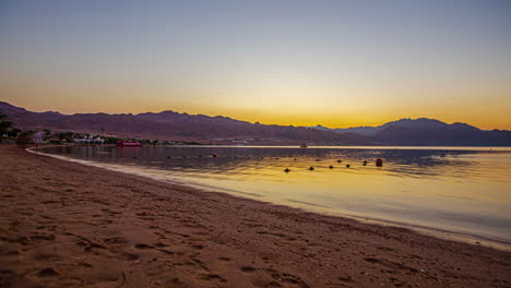 Timelapse-of-beautiful-sunrise-over-mountains-as-tourists-enjoy-stroll-on-beach