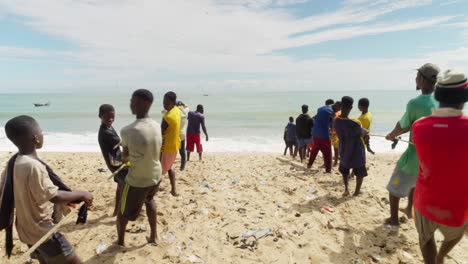 Boys-and-men-pull-fishing-net-out-of-ocean-to-beach-in-Moree,-Ghana