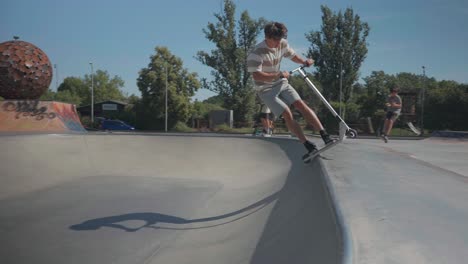 Young-stunt-scooter-rider-without-helmet-protection-slide-on-skatepark-bowl-edge