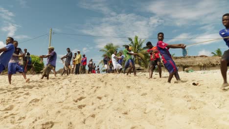 Frontal-view-of-young-men-pulling-up-fishing-net-to-sand-beach,-Ghana