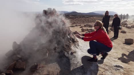 Female-tourist-warming-up-to-smoking-fumarole-in-Námafjall-Hverir-geothermal-area-in-Northeast-Iceland