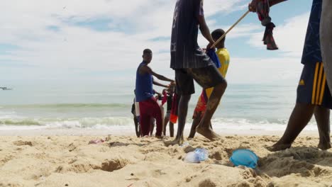 Men-and-boys-pull-fishing-net-by-rope-to-beach-in-Ghana,-ground-view
