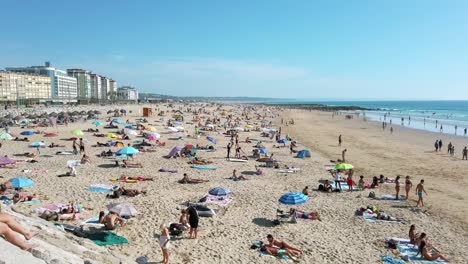 Crowded-Praia-do-Tarquínio-Paraíso-beach-with-Praia-do-Dragão-Vermelho-and-Praia-Nova-beaches-in-the-background-in-Costa-da-Caparica,-Portugal