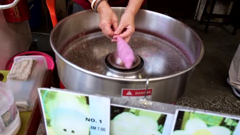 A-confectionery-expert-is-demonstrating-the-art-of-crafting-cotton-candy-at-the-entrance-of-an-alley-in-Old-Town-Ipoh,-Malaysia,-attracting-the-attention-of-passersby