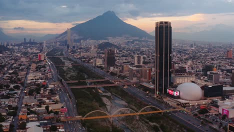 Amazing-sunset-view-of-Monterrey,-Mexico-with-bridges-over-the-Santa-Catarina-river-and-buildings-filling-the-sprawling-city-in-a-valley-surrounded-by-tall-mountain-peaks