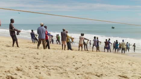 Men-pull-ropes-to-fishing-net-from-sea-to-sand-beach-in-Moree,-Ghana