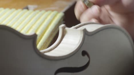 macro-close-up-of-artisan-luthier-maker-work-on-new-classic-handmade-raw-violin-smooth-edge-in-waist-and-purfling-rasp-in-workbench-of-workshop-in-Cremona-Italy-4k-video