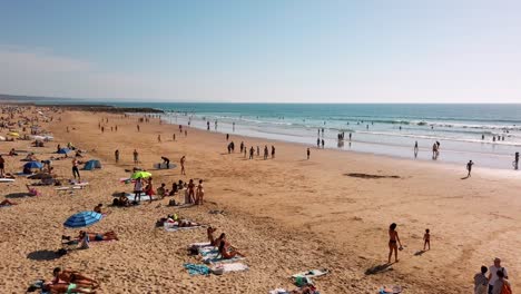 Sunbathing-and-swimming-people-at-Praia-do-Tarquínio-Paraíso-beach-in-autumn,-Costa-da-Caparica,-Portugal