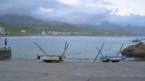 Fisherman-and-beached-rafts-at-a-boat-ramp-with-mountains-and-cloudy-sky-in-background,-filmed-in-wide-as-establishing-shot