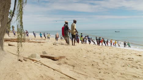 Wide-view-of-many-men-pulling-fishing-net-to-shore-on-beach-in-Ghana