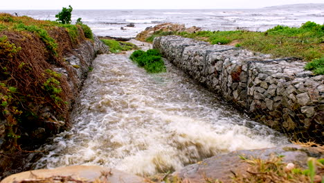 Rainwater-runoff-gushing-out-of-stormwater-drain-with-gabion-walls-toward-ocean