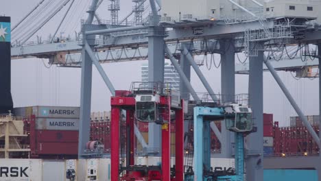 Zwei-Kräne-Fahren-Mit-Schiffscontainern-Im-Hafen-Von-Aarhus,-Im-Hintergrund-Ein-Maersk-Schiff