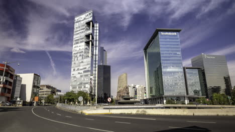 Panoramic-shot-of-the-Petroleos-Fountain-on-Paseo-de-la-Reforma-Avenue-with-several-office-buildings-in-the-background-on-a-sunny-day-in-Mexico-City,-several-vehicles-pass-in-front-of-it-on-the-avenue