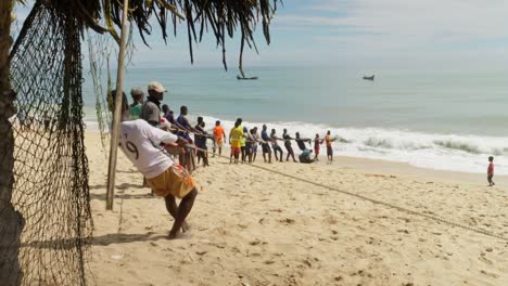 Men-stand-in-line-and-pull-fishing-net-from-sea-to-sand-beach-in-Ghana