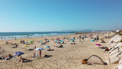 Beautiful-crowded-shoreline-of-Costa-da-Caparica-beach-with-full-of-people-in-autumn,-Portugal
