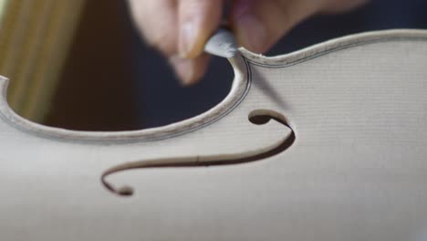 macro-close-up-of-artisan-luthier-maker-work-on-new-classic-handmade-raw-violin-smooth-edge-in-waist-and-purfling-rasp-in-workbench-of-workshop-in-Cremona-Italy-4k-video