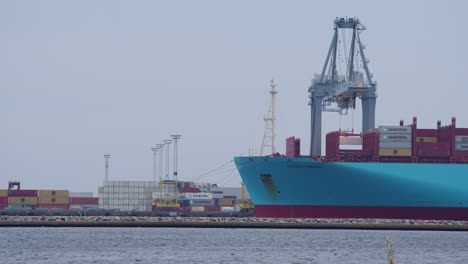 Maersk-cargo-ship-being-loaded-with-containers-while-cranes-are-delivering-them