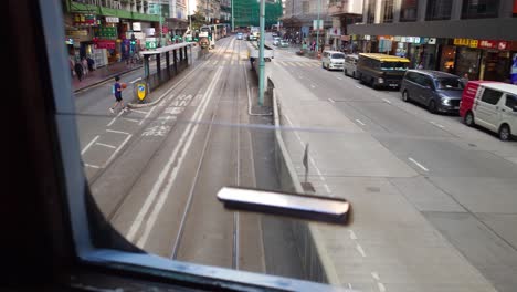 POV-Window-View-From-Back-Of-2nd-Deck-Of-Tram-Driving-Departing-Stop-In-Downtown-Hong-Kong