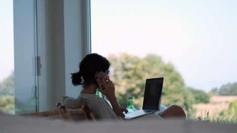 Mujer-Trabajando-Remotamente-En-Una-Computadora-Portátil-Con-Teléfono-En-Una-Casa-Moderna