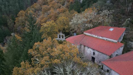 Circular-drone-aerial-shot-of-an-old-monastery-construction-surrounded-by-trees-and-nature-with-a-Christian-cross-on-top-and-red-roofs
