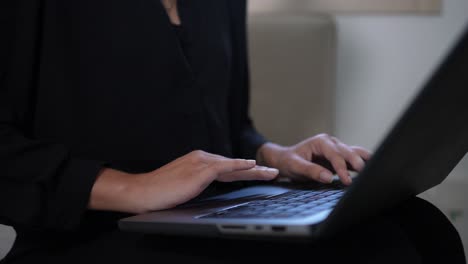 Hand-detail-shot-close-up-black-dressed-woman-working-with-a-laptop-on-the-sofa-of-her-house