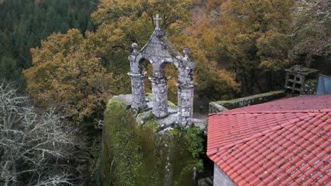 Aerial-drone-shot-of-an-old-monastery-construction-surrounded-by-trees-and-nature-with-a-Christian-cross-on-top