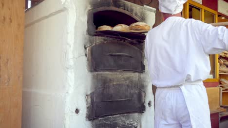 Baker-takes-loaves-of-bread-out-of-an-oven-at-the-Christmas-market-in-Meran---Merano,-South-Tyrol,-Italy