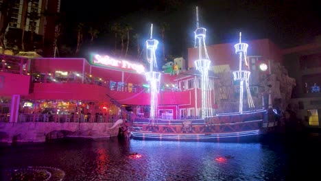 Un-Fascinante-Barco-Pirata-Iluminado-Con-Luces-De-Neón-Se-Erige-Como-Un-Faro-De-Entretenimiento-En-El-Strip-De-Las-Vegas,-Ofreciendo-Un-Espectáculo-De-Luces-Contra-La-Noche-Que-Captura-La-Vibrante-Escena.