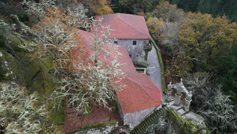 Aerial-drone-shot-of-an-old-monastery-construction-surrounded-by-trees-and-nature-over-the-mountains-with-a-Christian-cross-on-top