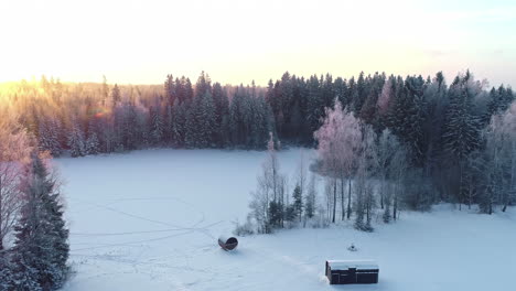 Sunset-over-a-frozen-lake-and-sauna-and-cabin-trailer-in-the-winter-countryside