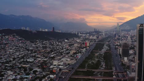 Aerial-view-of-river-cutting-through-city-of-Monterrey,-Mexico-with-vibrant-sunset-background