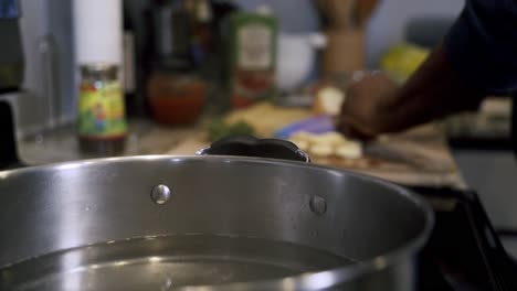 Kochendes-Wasser-Im-Topf-Im-Vordergrund-Mit-Zerkleinerten-Zutaten-Im-Hintergrund