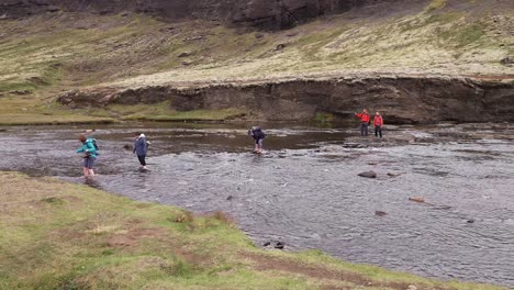 People-crossing-River-Botnsa-with-bare-feet-in-cold-water-on-top-of-Glymur-Waterfall