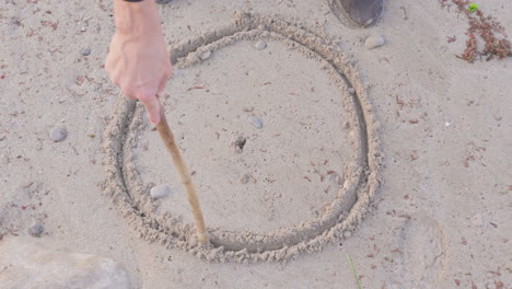 An-artist-meticulously-creates-a-perfect-circle-in-the-soft-sand-with-a-weathered-wooden-stick,-demonstrating-the-beauty-and-precision-that-can-be-achieved-through-simple-tools-and-techniques
