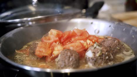 Adding-and-cooking-tomatoes-in-steel-pan-full-of-beyond-meatballs-Preparing-ingredients-to-make-vegan-beyond-meatballs-with-spaghetti-and-meat-sauce