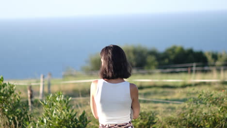 Woman-gazing-at-ocean-from-lush-hillside-during-summer