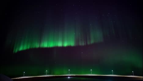 Dancing-aurora-borealis-at-night-time-over-a-illuminated-bridge-in-Scandinavia